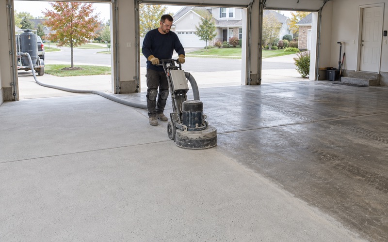 A walk-behind grinder opening up a Crystal Lake garage slab, the ground half pale and the rest still sealed.